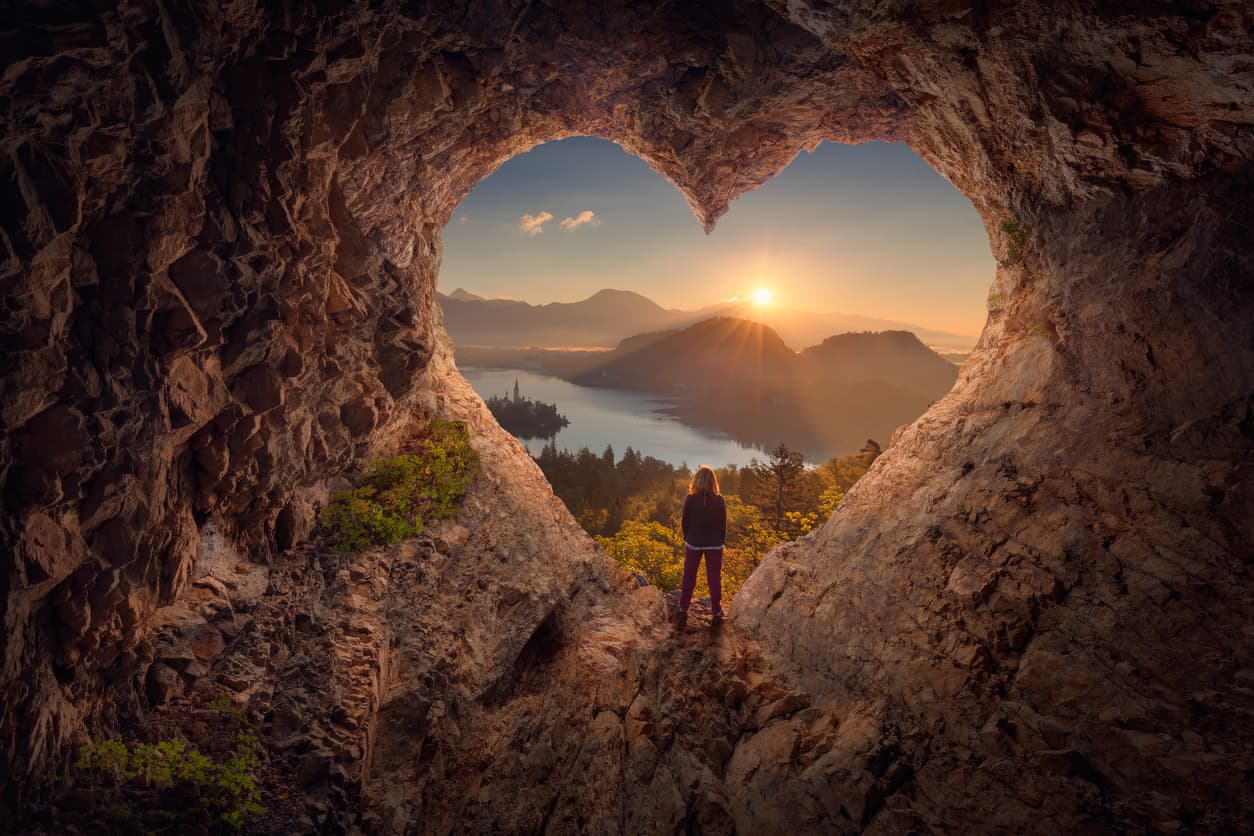 A person standing within a heart-shaped opening at sunrise